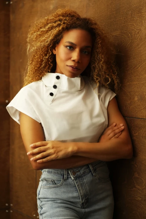 Daisi Jo — in a white button-neck top and jeans with her arms crossed