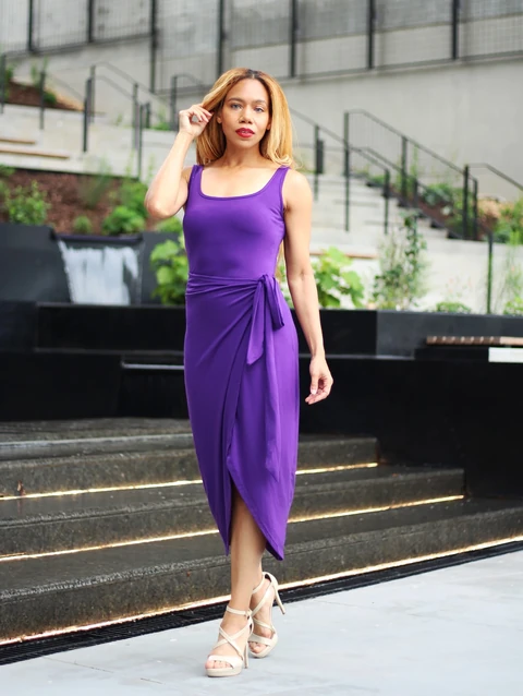 Daisi Jo modeling a purple wrap dress with one hand in her hair
