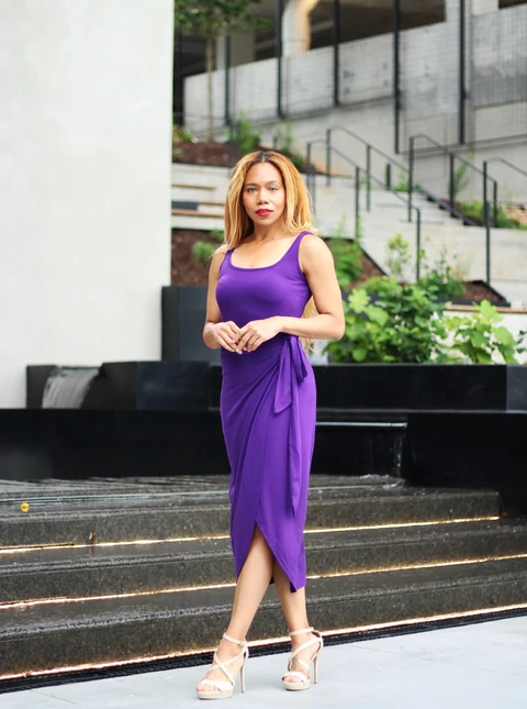 Daisi Jo posing in a purple wrap dress and cream heels with hands together