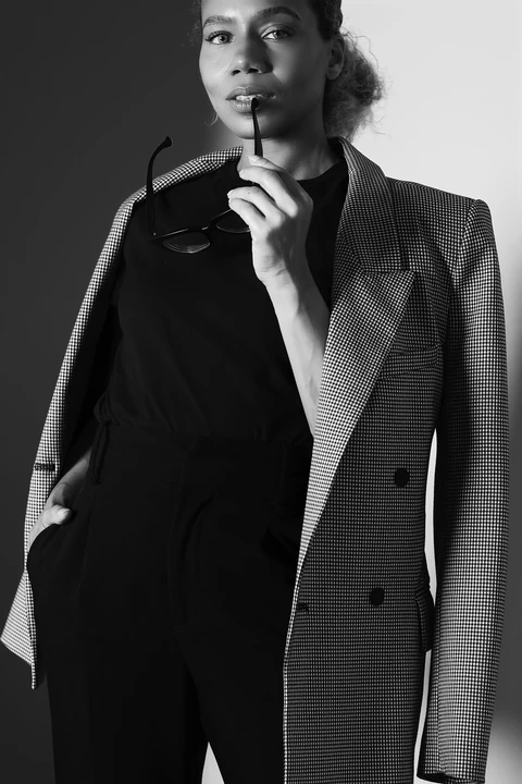 Daisi Jo modeling a checked blazer with glasses held at her lips