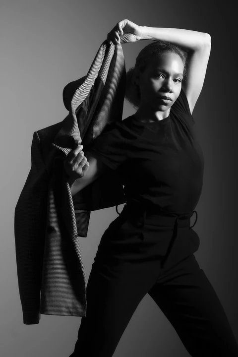 Black-and-white fashion portrait of Daisi Jo holding a checked blazer overhead