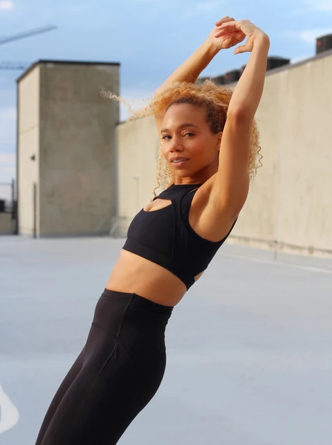 Daisi Jo stretching her arms overhead in black activewear outdoors